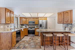 Kitchen with tasteful backsplash, brown cabinets, and light stone countertops