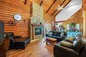 Living room featuring high vaulted ceiling, wood finished floors, a stone fireplace, a wooden ceiling with exposed beams, and ceiling fan
