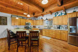 Kitchen with stainless steel appliances, light countertops, light wood-style flooring, decorative light fixtures, and a wooden ceiling with exposed beams