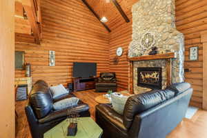 Living room with high vaulted ceiling, a stone fireplace, wood finished floors, a wooden ceiling with exposed beams, and log walls