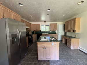Kitchen featuring stainless steel appliances, a center island, a textured ceiling, under cabinet range hood, and light brown cabinets