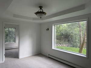 Spare room featuring baseboard heating, a tray ceiling, and light carpet