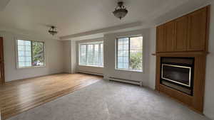 Unfurnished living room with a baseboard heating unit, carpet, and wood finished floors