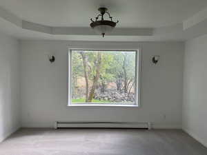 Unfurnished dining area featuring light colored carpet, a baseboard heating unit, and a tray ceiling
