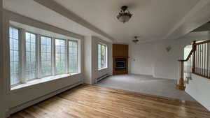 Unfurnished living room with a baseboard heating unit, light wood-style floors, a fireplace, and stairs