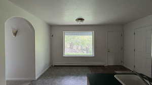 Unfurnished dining area featuring a textured ceiling, arched walkways, and a baseboard heating unit
