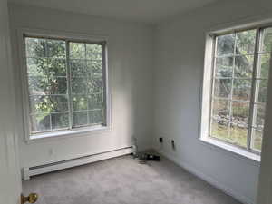 Carpeted empty room featuring a baseboard heating unit and healthy amount of natural light