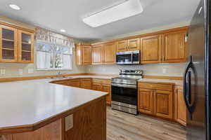 Kitchen featuring appliances with stainless steel finishes, brown cabinets, light countertops, glass insert cabinets, and recessed lighting