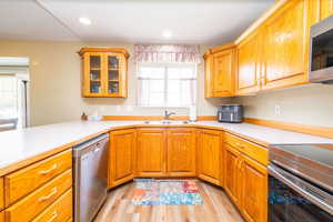Kitchen featuring light countertops, appliances with stainless steel finishes, glass insert cabinets, oak cabinets