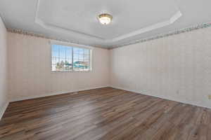Unfurnished room with a raised ceiling, light wood-style floors, and a textured ceiling