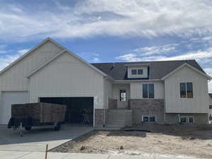 View of front facade featuring roof with shingles, stone siding, a garage, board and batten siding, and concrete driveway