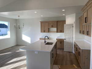 Kitchen with light stone counters, dark wood finished floors, an island with sink, recessed lighting, and a chandelier