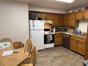 Kitchen with light countertops, appliances with stainless steel finishes, brown cabinetry, under cabinet range hood, and dark wood-style floors
