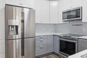 Kitchen with appliances with stainless steel finishes, white cabinets, gray cabinetry, light wood-style flooring, and light stone countertops