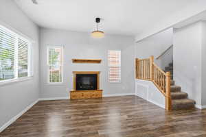 Unfurnished living room featuring stairway, dark wood-style flooring, and a glass covered fireplace