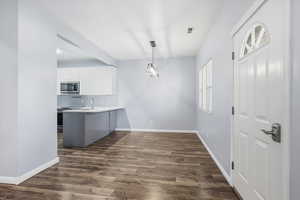 Kitchen featuring light countertops, white cabinetry, dark wood-type flooring, decorative light fixtures, and a peninsula