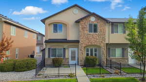 View of front facade featuring a fenced front yard, stone siding, and stucco siding