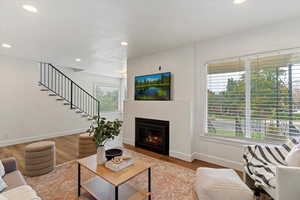 Living room with a lit fireplace, wood finished floors, recessed lighting, and stairway