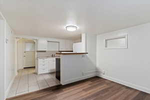 Kitchen featuring white cabinets, light wood-style floors, arched walkways, light countertops, and a peninsula