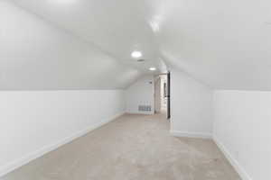 Additional living space with light colored carpet and vaulted ceiling