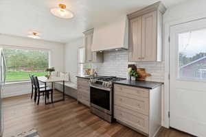 Kitchen featuring dark countertops, gray cabinetry, stainless steel appliances, premium range hood, and decorative backsplash