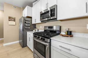 Kitchen with stainless steel appliances, gas stove and oven, white cabinetry, light stone counters, and light wood-style floors