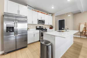 Kitchen featuring appliances with stainless steel finishes, white cabinetry, light wood-style floors, a center island with sink, and recessed lighting