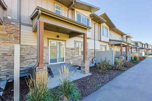 Back doorway and patio to property with board and batten siding, covered porch, stone siding, and a residential view