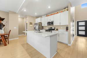 Kitchen with white cabinetry, appliances with stainless steel finishes, a center island with sink, light wood finished floors, and recessed lighting