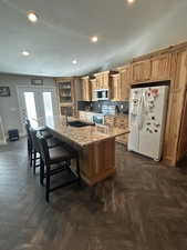 Kitchen with white appliances, a center island with sink, light stone countertops, recessed lighting, and a textured ceiling