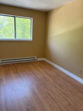 Unfurnished room featuring light wood finished floors, a baseboard radiator, and a textured ceiling