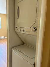 Laundry room with estacked washer and dryer, wood finished floors, baseboard heating, and a textured ceiling