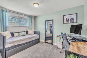 Carpeted bedroom featuring a textured ceiling and an office area