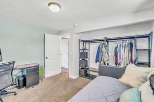 Carpeted bedroom with a closet, a textured ceiling, and a desk