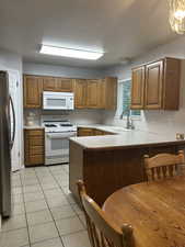 Kitchen featuring white appliances, light countertops, brown cabinetry, a peninsula, and a textured ceiling