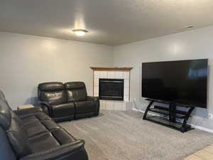 Living area with a tiled fireplace, a textured ceiling, and light colored carpet