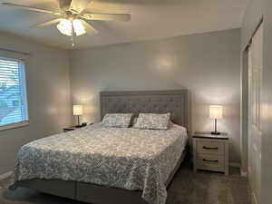 Bedroom with dark carpet, ceiling fan, and a closet