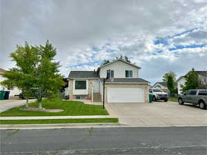 View of front facade with a front yard, concrete driveway, an attached garage, and roof with shingles
