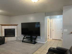 Living room featuring a textured ceiling, a tile fireplace, light tile patterned floors, and light carpet