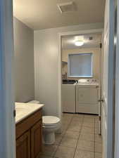 Bathroom with a textured ceiling, vanity, separate washer and dryer, and light tile patterned flooring