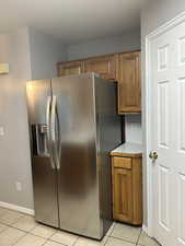 Kitchen with stainless steel fridge with ice dispenser, brown cabinets, light tile patterned flooring, and light countertops
