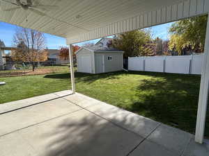 Fenced backyard with a patio area, ceiling fan, and a storage shed