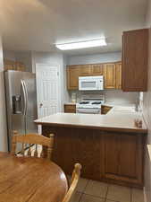 Kitchen featuring light countertops, white appliances, a peninsula, and brown cabinets