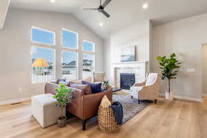 Living area with a stone fireplace, light wood finished floors, high vaulted ceiling, a ceiling fan, and recessed lighting