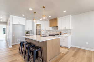 Kitchen with white cabinets, tasteful backsplash, light wood-style floors, pendant lighting, and recessed lighting