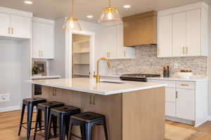 Kitchen featuring white cabinetry, backsplash, light wood-type flooring, hanging light fixtures, and recessed lighting