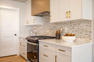 Kitchen featuring gas range oven, white cabinetry, decorative backsplash, light wood-style flooring, and modern cabinets
