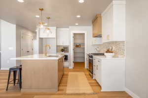 Kitchen with white cabinetry, a kitchen island with sink, a kitchen breakfast bar, decorative backsplash, and recessed lighting