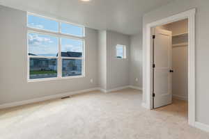 Unfurnished bedroom featuring light colored carpet and a walk in closet