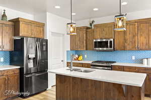 Kitchen with appliances with stainless steel finishes, decorative light fixtures, brown cabinets, a center island with sink, and recessed lighting